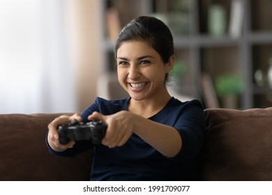 Video gamer. Passionate excited indian female teenager play favorite console videogame spending weekend at home alone. Overjoyed young ethnic lady sit on couch hold controller engaged in computer game