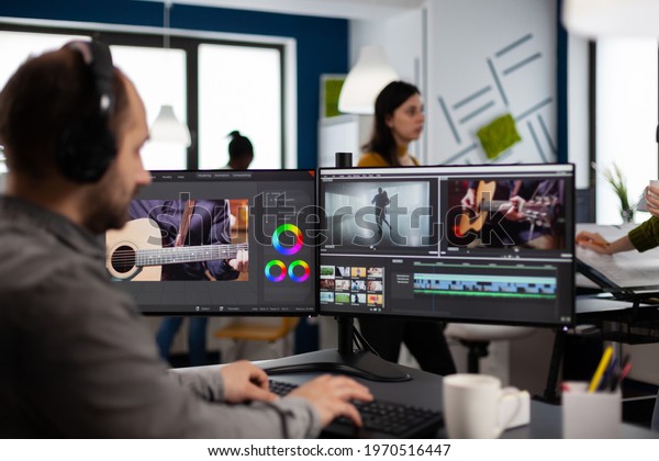 Video maker listening music at headphones editing\
movie using post production software working in creative agency\
office. Videographer processing audio film montage on computer in\
multimedia company
