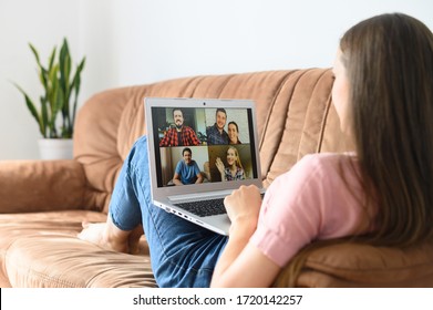 Video meeting, online conference with coworkers. A young woman is using laptop app for video communication with several people together while relaxed lays on the sofa at home