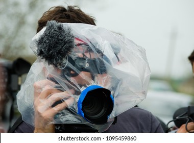 Video Operator Journalist Filming An Event During The Rain With A Plastic Bag Wrapped Around His Camera. Concept Of Pritecting The Gear From Getting Wet