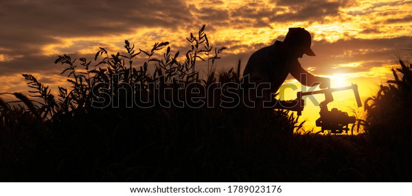 Video Operator with Modern Camera Installed on a\
Gimbal Walking Along Countryside During Scenic Sunset. Panoramic\
Silhouette Concept.