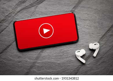 Video player app on phone's screen and wireless earphones on dark background