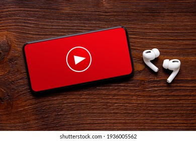 Video player icon on the screen of mobile phone and modern wireless earbuds on dark wooden surface