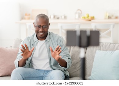 Video Recording For Modern Blog As A Remote Work Or Hobby. Mature Black Man Looking In Smartphone Camera On Tripod, Sitting On Sofa In Living Room Interior During Covid-19 Pandemic, Copy Space