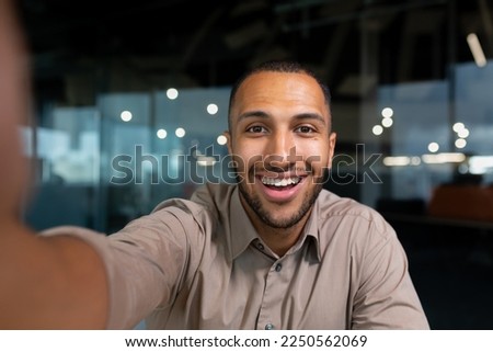 Video ringing, successful businessman looking at smartphone camera talking remotely with colleagues, Hispanic man smiling at work inside office, webcam view pov.
