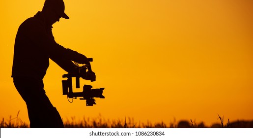 Video Stabilizer Operator. Taking Video Shoots Using DSLR Gimbal Equipment. Sunset Silhouette Concept.