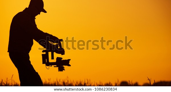 Video Stabilizer\
Operator. Taking Video Shoots Using DSLR Gimbal Equipment. Sunset\
Silhouette Concept.