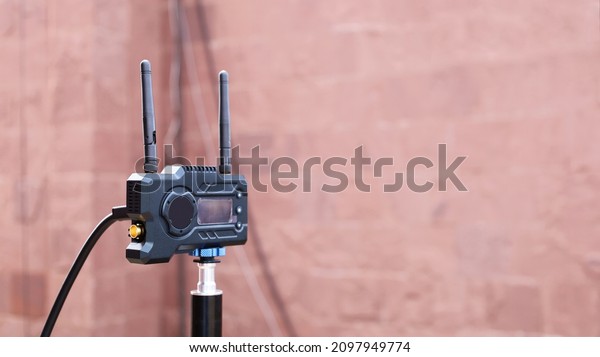 Video\
transmitter and receiver. Black transmitter of wireless video\
transmission system on a metal pole with red-brown brick wall\
background with copy space. Selective\
focus