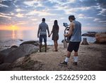 Videographer, camera and couple for sunset photoshoot, video analysis or travel documentary filming. Production process, person and recording for beach, movie or filmmaking with professional gear