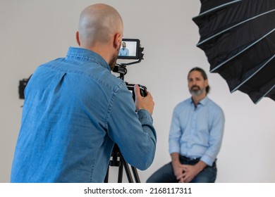 Videographer Or Camera Man Is Filming Male In Front Of Camera And Lighting. Behind The Scenes On Corporate Video Production Set. 