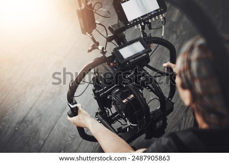 Videographer, camera and man filming in studio for photography, production and media. Behind the scenes, backstage and person with stabilizing equipment on set shooting videos, documentary or film