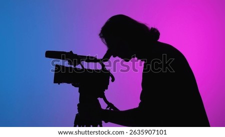 A videographer is captured in silhouette while filming in a studio environment with gradient lighting.