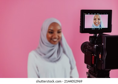 Videographer in digital studio recording video on professional camera by shooting female Muslim woman wearing hijab scarf plastic pink background. - Powered by Shutterstock