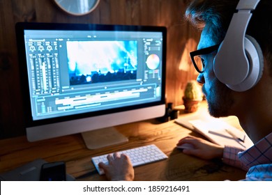 Videographer editor film maker wears headphones using digital software on desktop computer editing video footage content working using post production multimedia making montage, over shoulder view.