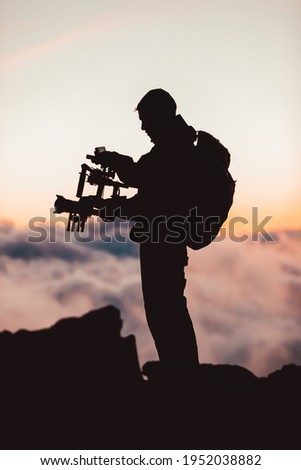Videographer man shooting footage using dlsr camera mounted on gimbal stabilizer equipment. Video production crew for movie, cinema. Silhouette of professional filmmaker filming outdoor.
