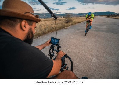 A videographer recording a triathlete riding his bike preparing for an upcoming marathon.Athlete's physical endurance and the dedication required to succeed in the sport. - Shutterstock ID 2291345057