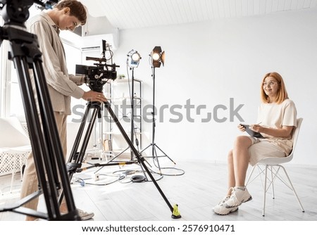 Videographer work. Interview studio. Female art director sitting on chair notebook in hands. Smiling girl poses video photo scene.