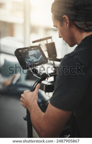 Videography, camera and man filming in studio for photography, production and media. Behind the scenes, backstage and person with stabilizing equipment on set shooting videos, documentary and film