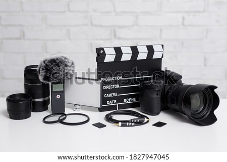 videography concept - modern dslr camera, lenses, microphone, led light, clapper board and other videography equipment over white brick wall background