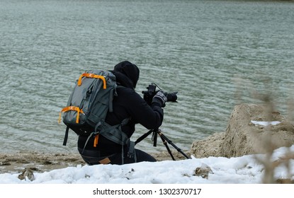 Videomaker With Camera On The Shores Of The Lake In The Mountains In The Snow In Winter - Concept Of Documentary Filmmaking In Extreme Conditions - Passion For Work