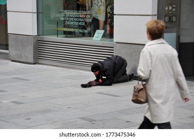 VIENNA / AUSTRIA - APRIL 11 2012: A Woman Walks Past A Beggar Man, Who Prostrates Himself With His Hat Out For Donations, On Pedestrian Mall Kärntner Straße.