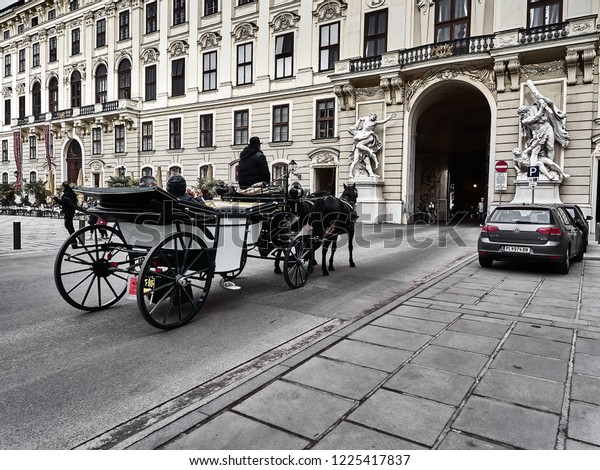 Vienna, Austria - November 1, 2018 - A horse-drawn\
carriage passing inside the Hofburg palace. People are visiting the\
palace
