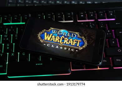 Viersen, Germany - January 9. 2021: Closeup of smartphone screen with logo lettering of online game world of warcraft on illuminated computer keyboard (focus on center of central lettering)