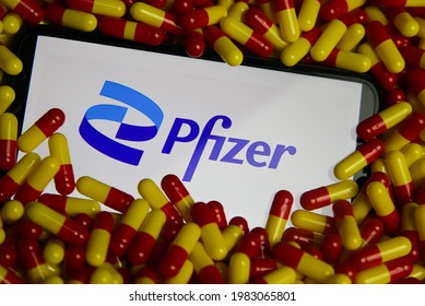 Viersen, Germany - May 9. 2021: Closeup of mobile phone screen with logo lettering of Pfizer pharmaceutical company in pile of pills (focus on center of word Pfizer)