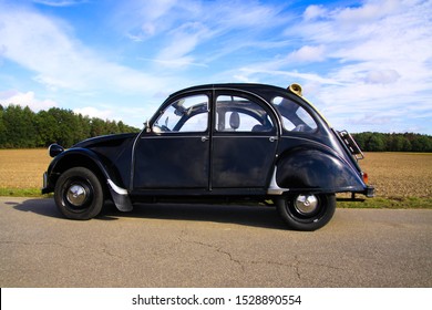Viersen, Germany - October 12. 2019: Side View Of Black French Classic Cult Car 2CV Citroen With Open Roof In Rural Area Against Blue Sky 