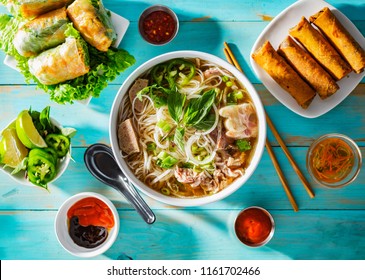 vietnamese beef pho bo soup in bowl on table top with spring rolls and appetizers