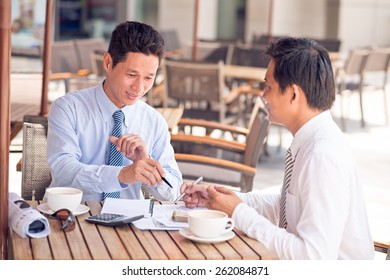 Vietnamese business partners discussing documents while sitting in a cafe