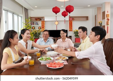 Vietnamese family chatting and eating at Tet celebration; couplets with best wishes for coming year in the background