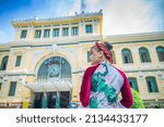 Vietnamese girl in traditional Ao Dai dresses taking photos in front of the post office in Ho Chi Minh city (Saigon), Vietnam. Travel concept.