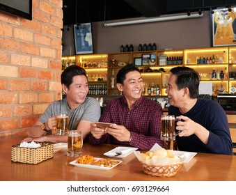 Vietnamese mature men laughing and drinking beer in pub - Powered by Shutterstock