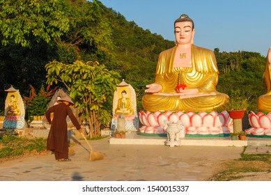 Vietnamese Monk Sweeping By Golden Buddha Statues Of Dao Temple In Nha Trang, Vietnam 