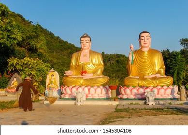 A Vietnamese Monk Sweeping By Two Golden Statues Of Buddha In Dao Temple In Nha Trang, Vietnam 