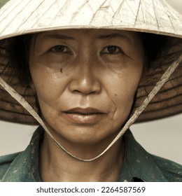 vietnamese peasent whereing traditional pointed hat with large expressive eyes looking directley at viewer