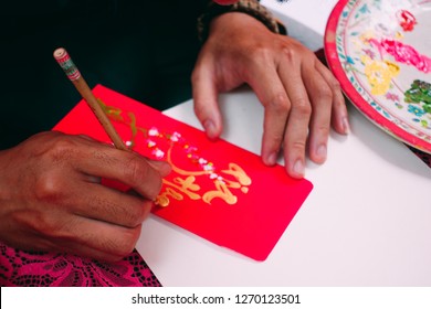 Vietnamese Scholar Write Calligraphy On Red Envelope, Ang Pow in Lunar New Year. Calligraphy Festival Is A Popular Tradition During Vietnam Tet Holiday. Calligrapher Draw Handwriting In Springtime