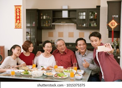 Vietnamese teenage boy taking selfie with his family at Tet celebration dinner. Scrolls wishing luck and wealth in the background
