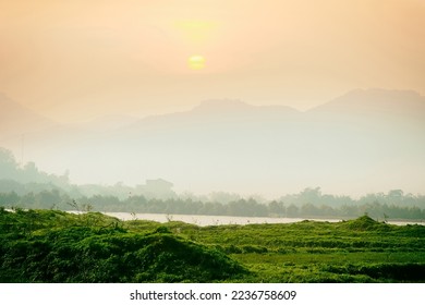 Vietnamese tropical nature (tropical winter). Forests, neadows and shrubs of the foothills, mountains on the horizon. The setting of the foggy sun - Shutterstock ID 2236758609