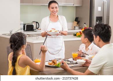 Vietnamese woman bringing dish to dinner table - Powered by Shutterstock