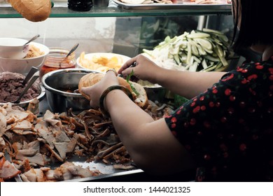 Vietnamese woman sell Vietnam bread on cart at night street food, stuffed food with meat, pork bologna, pickle, a famous and popular food that cheap, quick, Ho Chi Minh city