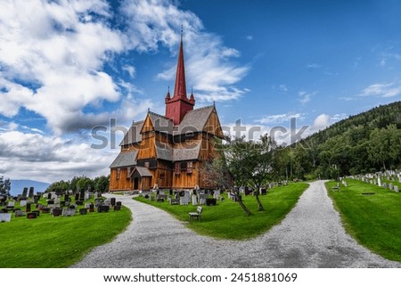 View of the 13th century historic Ringebu Stave Church stands amidst headstones under a blue sky with clouds in Summer, echoing centuries of Norwegian heritage.