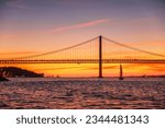 View of 25 de Abril Bridge famous tourist landmark of Lisbon connecting Lisboa and Almada over Tagus river with tourist yacht silhouette at sunset. Lisbon, Portugal