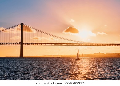 View of 25 de Abril Bridge famous tourist landmark of Lisbon connecting Lisboa and Almada on Setubal Peninsula over Tagus river with tourist yacht silhouette on sunset. Lisbon, Portugal - Powered by Shutterstock
