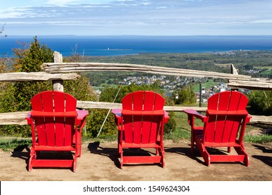View of 3 red muskoka chairs with Blue Mountain resort and village at the background during the autumn in Collingwood, Ontario