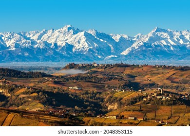 View from above of autumnal hills and snowy mountains on background under blue sky in Piedmont, Northern Italy.