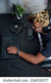 A View From Above Of A Black Guy Sitting At A Laptop, Talking Into A Microphone And Reading The News. A Black Man Communicates With Podcast Listeners In An Online Chat