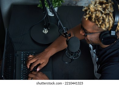 View From Above Of A Black Guy Sitting At A Laptop, Talking Into A Microphone And Reading The News. A Black Man Communicates With Podcast Listeners In An Online Chat