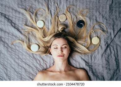 View from above of blond woman close eyes lying on bed with natural eco friendly solid shampoo bars or conditioners on her hair. Zero waste and sustainable plastic free lifestyle.